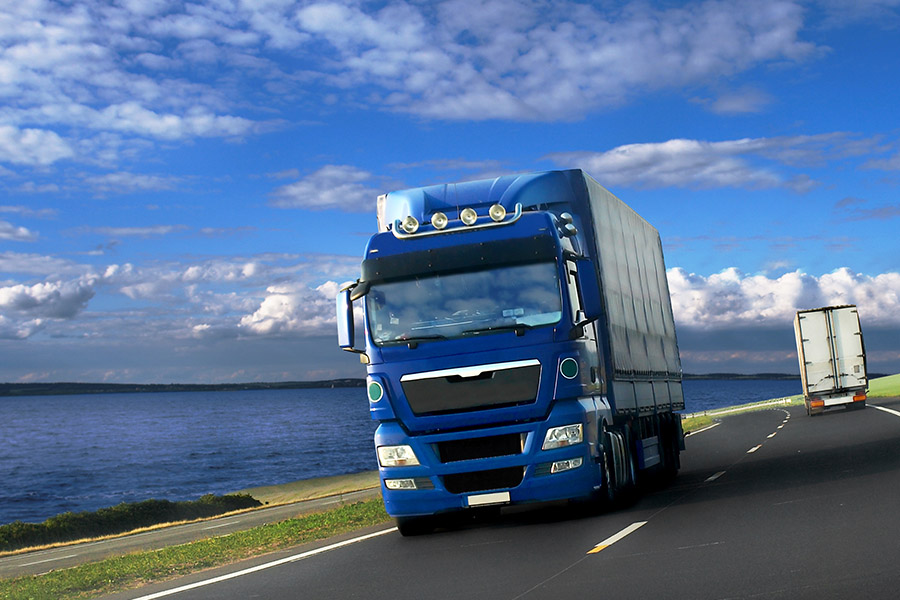 Business Insurance - A Blue Truck Drives on a Curved Road Alongside a Lake on a Sunny Day