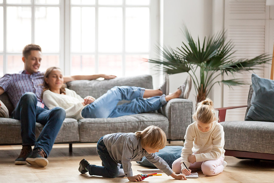 Personal Insurance - A Mother and Father Relax on a Sofa as They Watch Their Two Children do Artwork on the Floor at Home