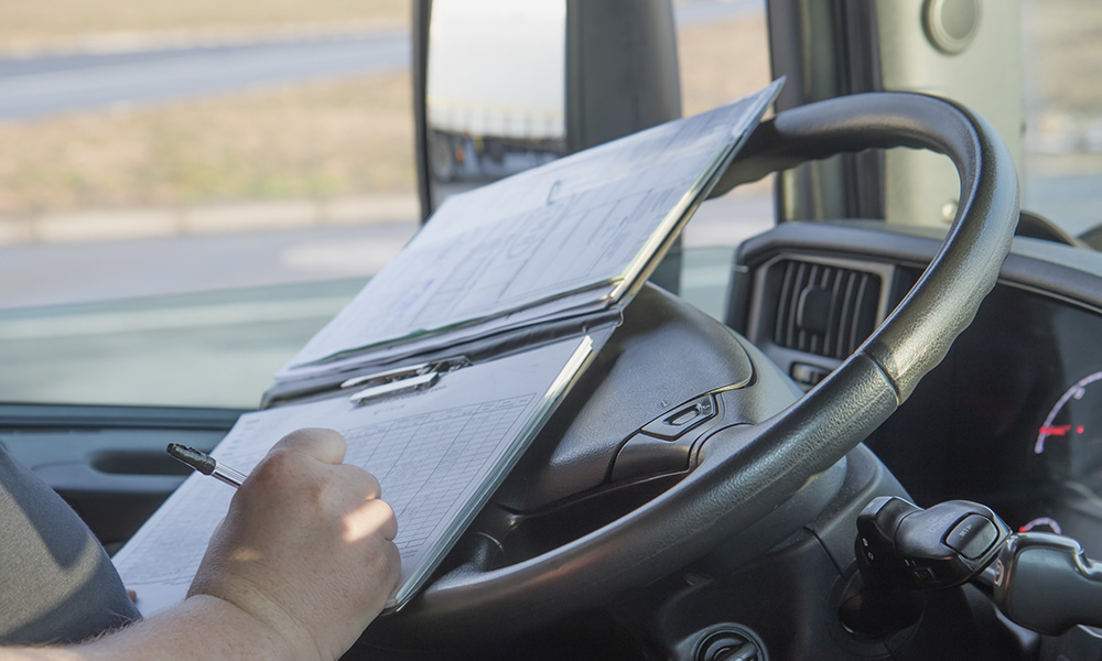Trucking Business Start-Up- Paper-work To Always Have In Your Truck - Truck Driver Parked and Working on Paperwork at the Wheel